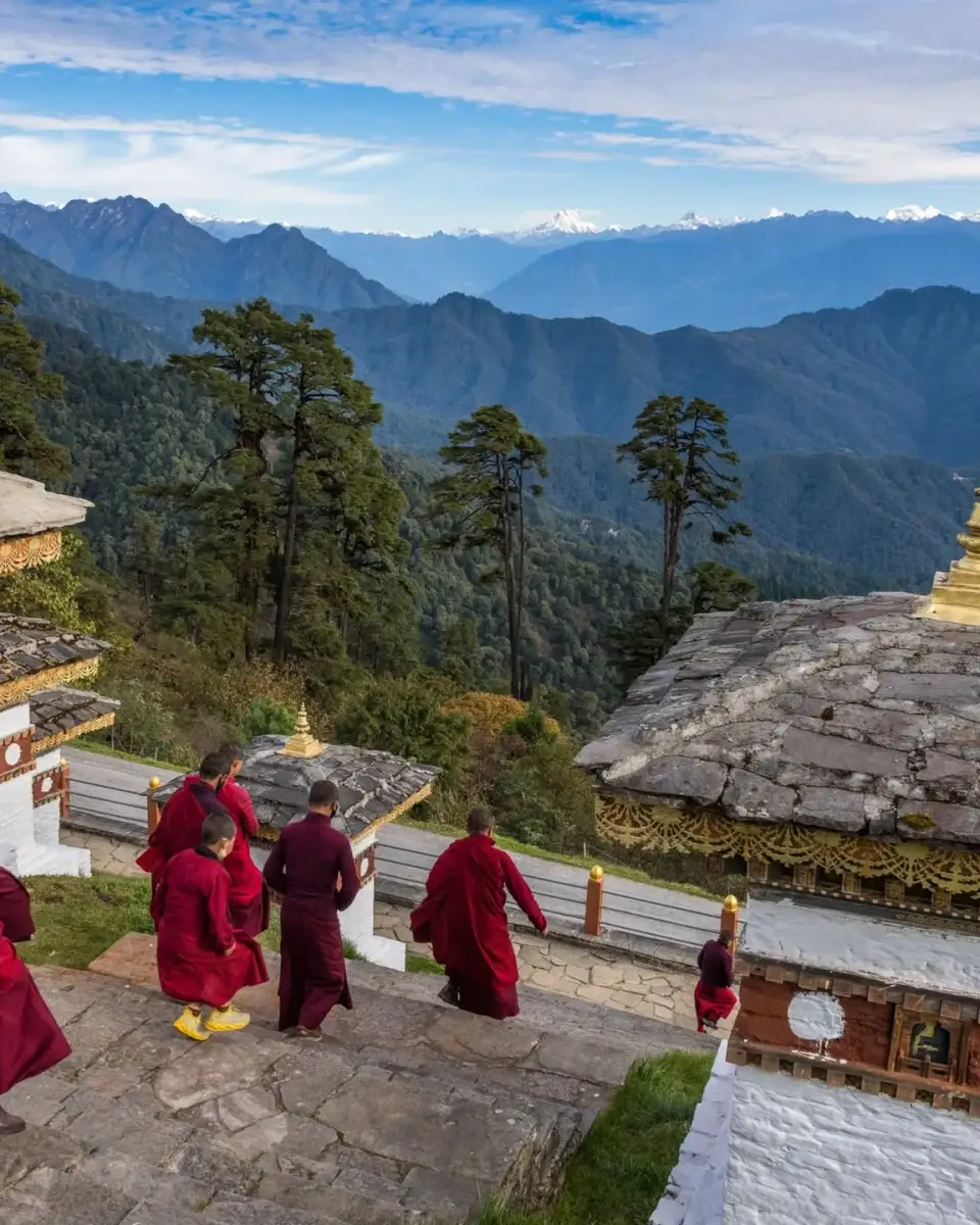 Monks in red robes among the 108 chortens at Dochula Pass, with the Himalayan range behind them