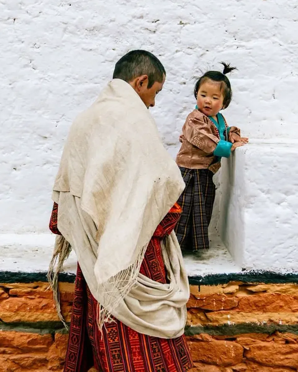 A Bhutanese man in a woven shawl greeting a young child